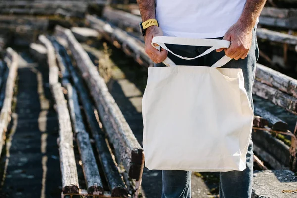 Jovem segurando saco eco têxtil branco contra fundo urbano da cidade. Conceito de ecologia ou de protecção do ambiente. Saco eco branco para simular . — Fotografia de Stock