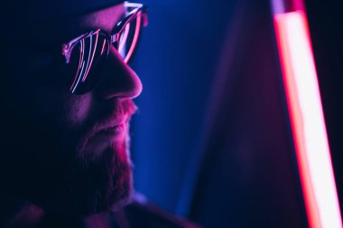 Şehir sokaklarında hipster yakışıklı adam Neon işaretler tarafından aydınlatılmış olmak. O siyah kap, kot pantolon ve güneş gözlüğü ile deri motosikletçi ceket veya asimetrik fermuar ceket giyiyor.