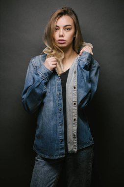 Gri arka planda kot pantolon giyen seksi sarışın bir kadının moda portresi.