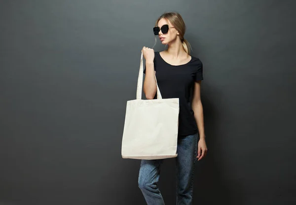 Ung kvinna som innehar vit textil Eco Bag mot grå bakgrund. Ekologin eller miljöskydds konceptet. Vit Eco Bag för mock-up. — Stockfoto