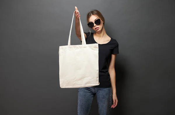 Jonge vrouw Holding witte textiel Eco-tas tegen grijze achtergrond. Ecologie of milieubescherming concept. Witte Eco-tas voor mock up. — Stockfoto