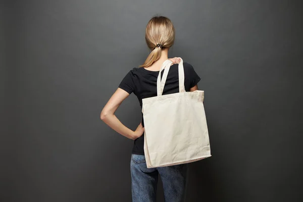 Wanita muda memegang tas eco tekstil putih dengan latar belakang abu-abu. Ekologi atau konsep perlindungan lingkungan. Kantong eco putih untuk mengejek . — Stok Foto