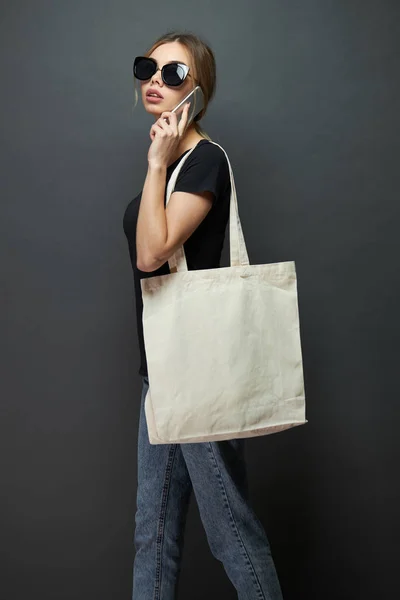 Ung kvinna som innehar vit textil Eco Bag mot grå bakgrund. Ekologin eller miljöskydds konceptet. Vit Eco Bag för mock-up. — Stockfoto