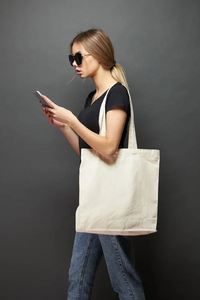 Jonge vrouw Holding witte textiel Eco-tas tegen grijze achtergrond. Ecologie of milieubescherming concept. Witte Eco-tas voor mock up. — Stockfoto