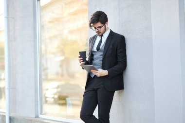 Genç iş adamı dışarıda tablet kullanıyor. Klasik bir takım elbise giyiyor.