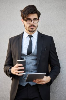 Genç iş adamı dışarıda tablet kullanıyor. Klasik bir takım elbise giyiyor.