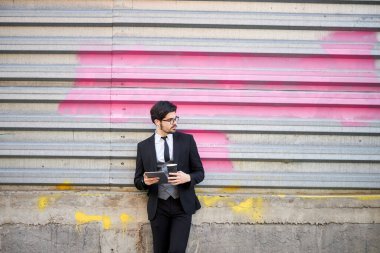 Genç iş adamı dışarıda tablet kullanıyor. Klasik bir takım elbise giyiyor.