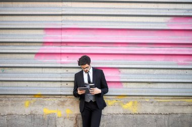 Genç iş adamı dışarıda tablet kullanıyor. Klasik bir takım elbise giyiyor.