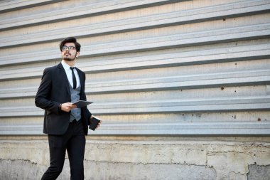 Genç iş adamı dışarıda tablet kullanıyor. Klasik bir takım elbise giyiyor.