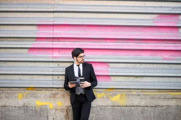 Genç iş adamı dışarıda tablet kullanıyor. Klasik bir takım elbise giyiyor.