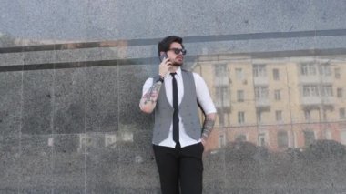 Şehir caddesinde, üzerinde şık giysiler olan bir iş adamı telefonda konuşuyor.