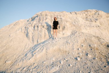 Gün batımında ince, güzel bir kız beyaz dağın üzerinden yazın güneşe bakıyor.