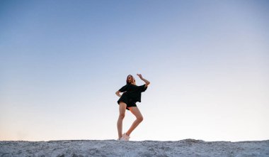 Gün batımında siyah giyinmiş, makyajlı seksi bir kadın. Güzel, uzun bacakları var.