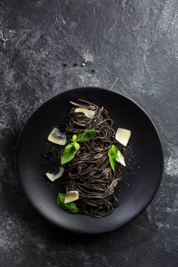 Siyah makarna (mürekkep balığı mürekkebi), limon biberi sosu, fesleğen yaprağı, siyah bir tabakta parmesan. Düz bir manzara. Dikey yönelim