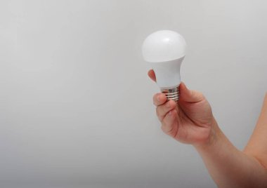 Adamın eli enerjiyi tutuyor. Gri arka planda ampulü kurtarıyor.