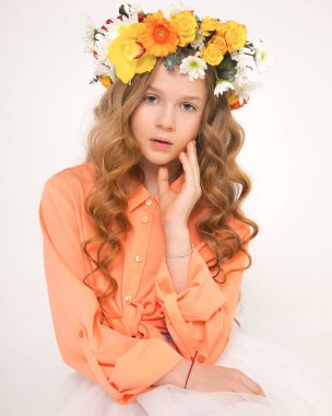 Stüdyo fotoğrafı. Uzun saçlı, güzel, kızıl saçlı, şık bukleli, beyaz arkaplan. Kafasında çiçek aksesuarı olan bir orman perisi. Sosyal ağlarda ya da web sitelerinde berber ürünlerinin reklamını yapmak