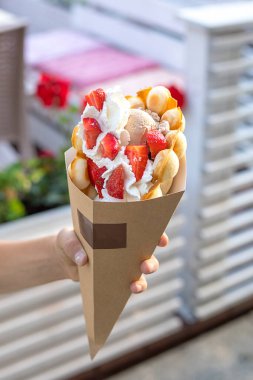 Belçika waffle 'ında bir şehir kafesinin arka planında çilek ve kremayla süslenmiş büyük, güzel bir dondurma. Yararlı ve zararlı yemek değil.