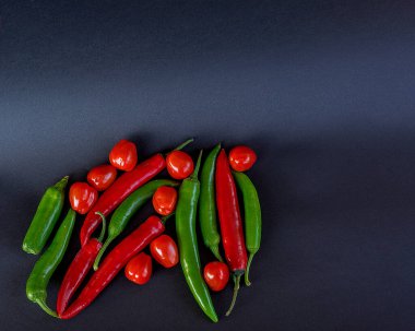 Vişneli domatesler ve siyah ahşap masadaki eski tabakta kırmızı kırmızı kırmızı biberler. Kırmızı biber ve domatesli koyu yiyecek fotoğrafçılığı. Fotoğraf.