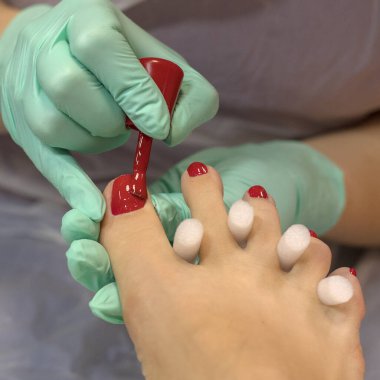 Genç bir kadın güzellik salonunda profesyonel kırmızı pedikür yaptırıyor..