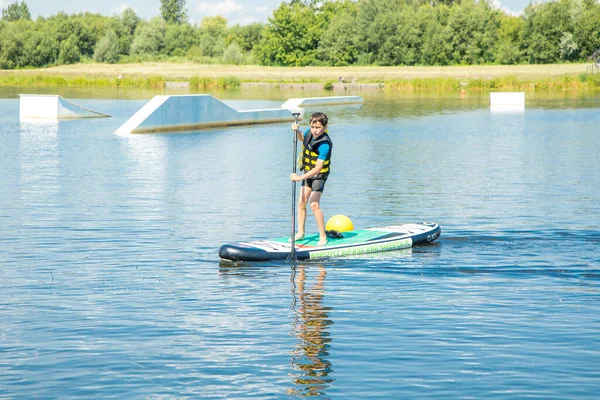 A paddler-boarder. Photo of 10-year-old Boy rowing on a standing Board. Healthy lifestyle. Water sports, SUP surfing tour in adventure camp on active summer sport camp. Healthy active lifestyle