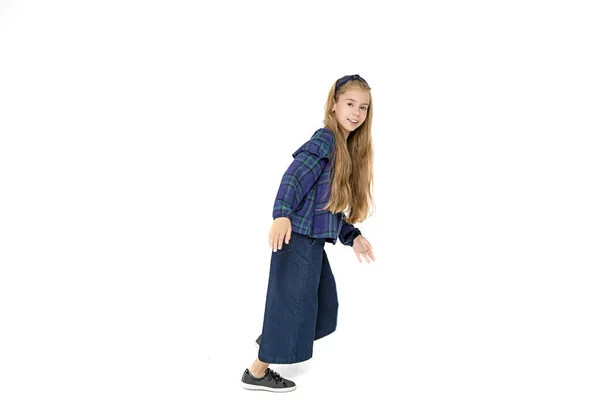 Beautiful school girl is having fun, running in fashionable blue school uniform on white background. Isolated. Dynamic full-length Photo. Autumn, knowledge, English language courses. Education, joy.