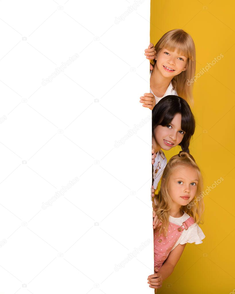 Group of three children of a girl with a white Board on a bright yellow background. Banner, free space for your ads, text. Billboard