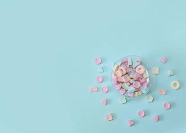 Yumuşak mavi arka planda küçük renkli şekerler dağılmış. Şekerleme, sağlıksız yiyecek aşkı. Diyet olsun. Kartpostal ya da kapak. Uzayı kopyala Tatil renkleri. Tasarım elemanları. Tatil, doğum günü konsepti