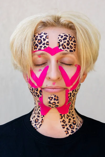 Güzel bir kadın, 45 yaşında, Kafkasyalı, estetik bantlama prosedürü. Bandın rengi leopar stili ve pembe. Spa salonu. Kırışıklık ve yorgunluğa karşı yaşlanma önleyici tedavi. Fotoğrafı kapat.