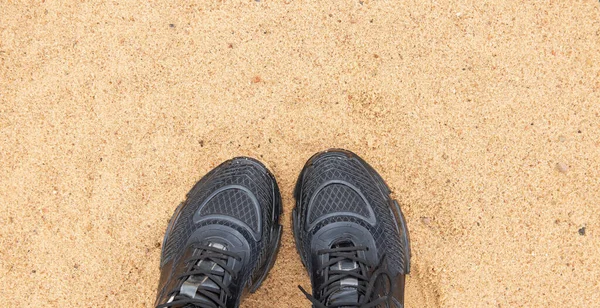 Scarpe da ginnastica nere su fondo sabbia. Il concetto di camminare e di sport. Vista dall'alto. Copia spazio per testo. Foto per blog, articolo o sito web — Foto Stock