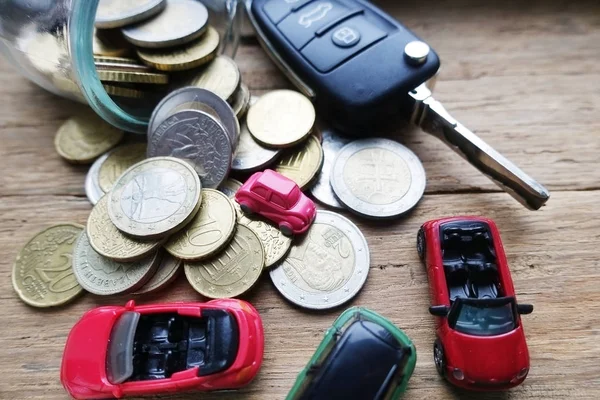 Car running cost as maintenance or insurance with toy cars, money savings and car key on wooden background