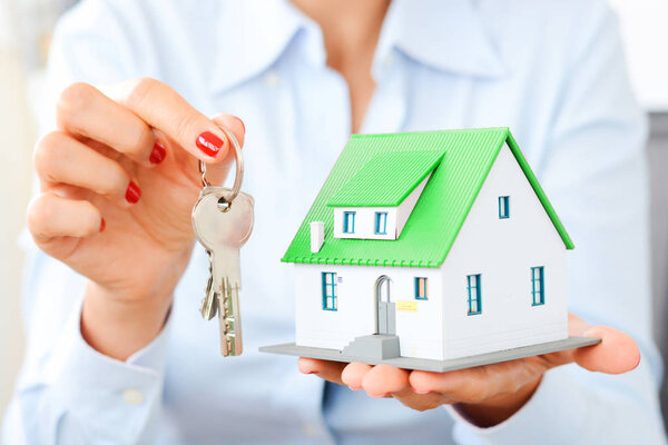 Businesswoman holding miniature house and key, real estate transaction concept