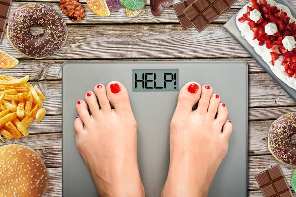 Feet of woman on weighting scale asking for help to avoid the temptation to eat unhealthy food