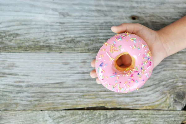 Childs Hand Met Aantrekkelijke Roze Donut Houten Tafel Als Achtergrond — Stockfoto