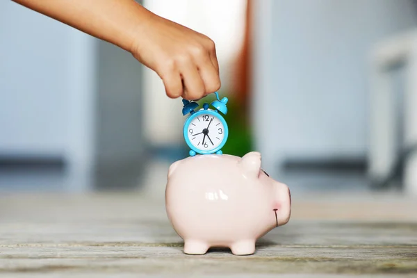Time is precious, save time concept with piggy bank and blue alarm clock in little girl hand