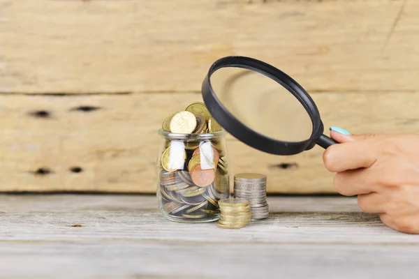 Analyzing personal savings or budget concept with jar full of money under the magnifying glass