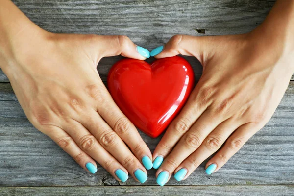 Heart health concept with womans hands protecting a shiny red heart