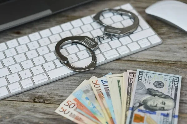 Money from online fraud concept, with cash banknotes near computer keyboard and handcuffs