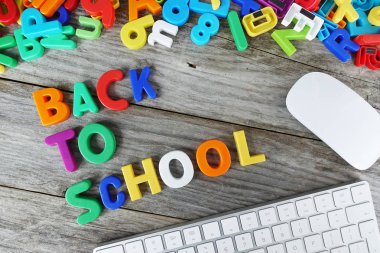 Bilgisayar klavyesi ve fare ile ahşap masa üzerinde plastik harf parçalarından okul metnine geri dön