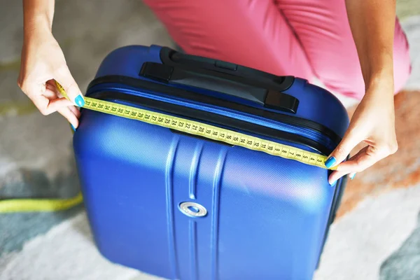 Young woman measuring travel luggage or suitcase before flight