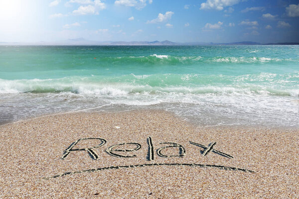 Расслабьтесь слово написано от руки на пляже песок с белым пером в летнее время
        