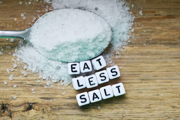 Eat less salt recommendation with plastic letters  and granulated salt on wooden chopping board