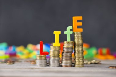 Life cost or cost of living concept with colourful letters on ascending piles of money clipart