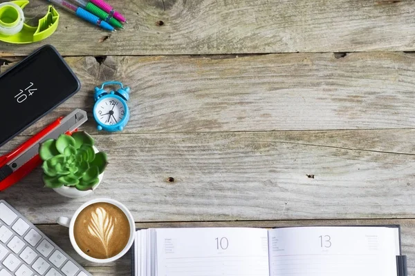Office supplies, coffee and green plant on the left side of wooden background
