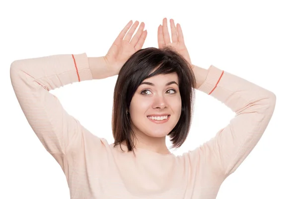 The girl shows the rabbit. Brunette shows ears for head. Portrait of smiling woman on white isolate background Stock Picture