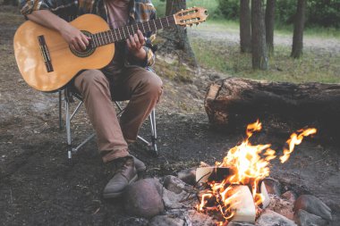 Ormanda kamp yapmak. İnsan doğada ateşin yanında gitar çalar. Yaz kampı. Doğada rahatlama
