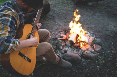 İnsan doğada ateşin yanında gitar çalar. Yaz kampı. Doğada rahatlama