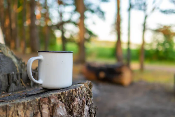 camping in the forest. White camping cup with tea on a forest background. summer camping