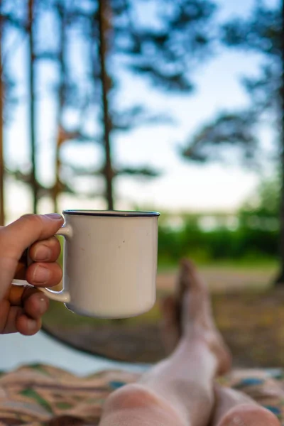 camping in the forest. White camping cup with tea on a forest background. summer camping