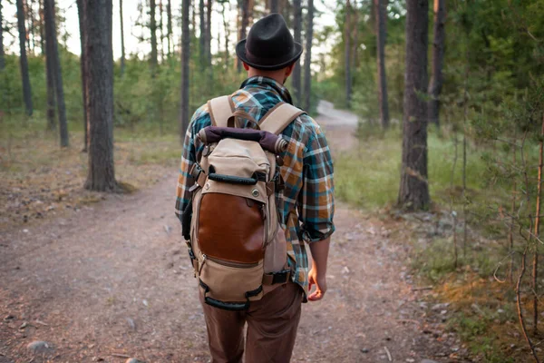 camping in the woods. a man in a hat with a backpack walks through the woods.
