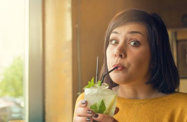 Sarı kazaklı esmer kokteyl içiyor. Lezzetli mojito. Kafede Mojito kokteyli içen güzel bir kız.